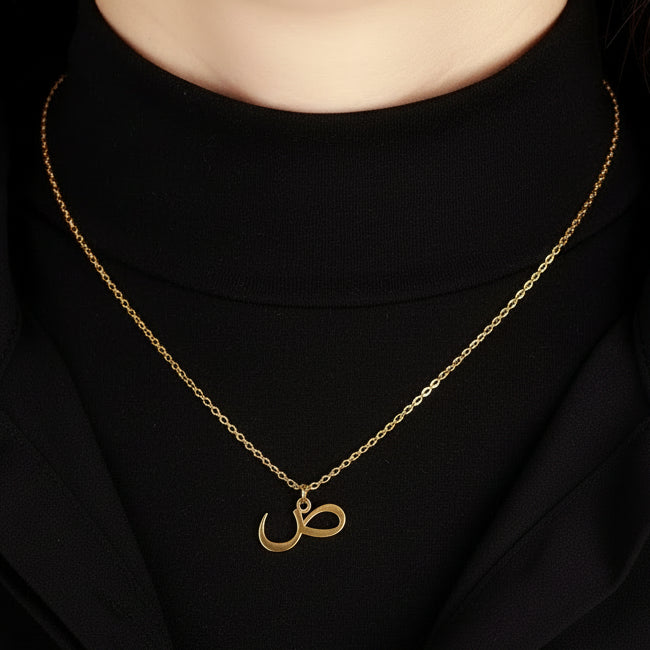 Gold necklace with a pendant worn by a person in a black shirt