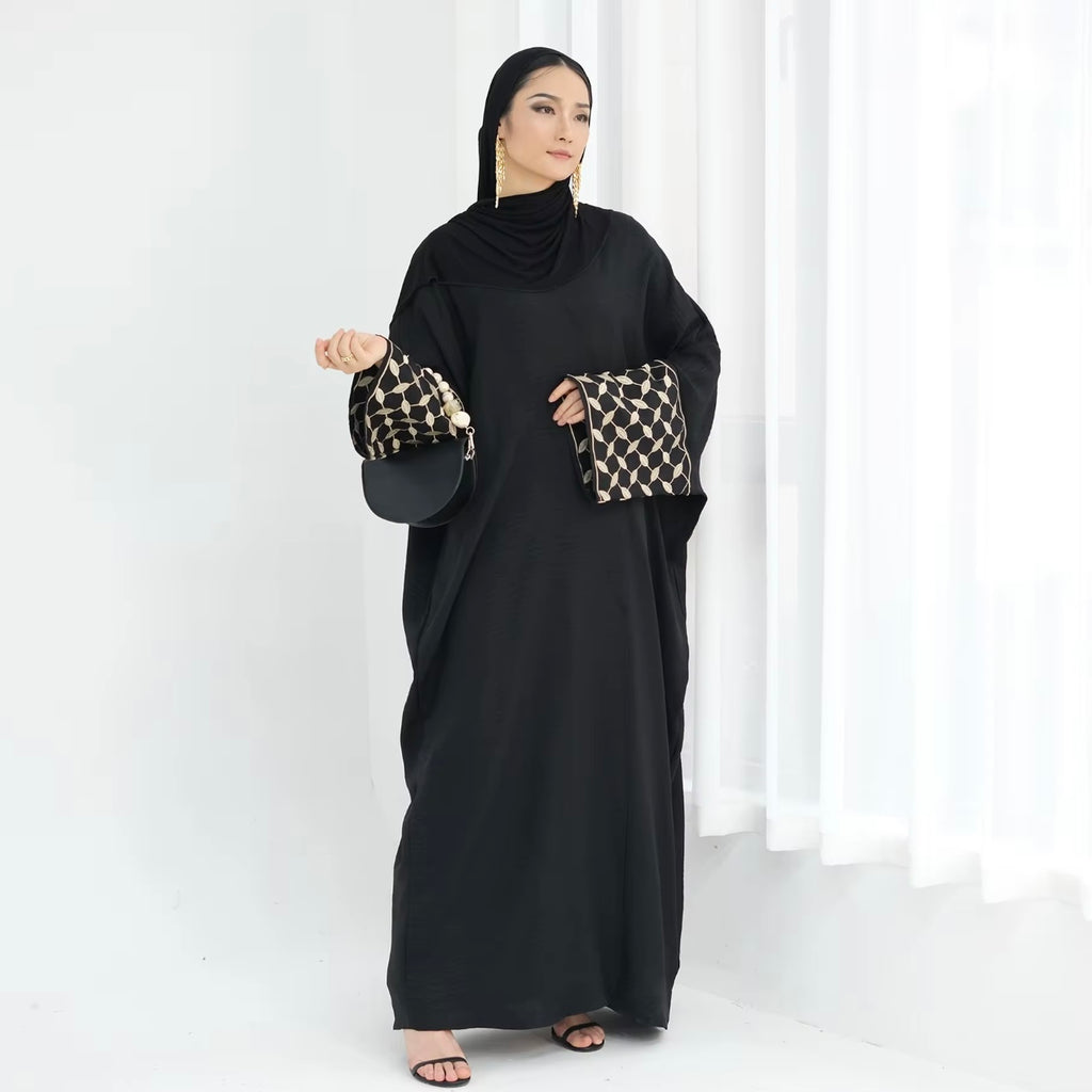 Woman wearing a black abaya with patterned sleeves against a white background