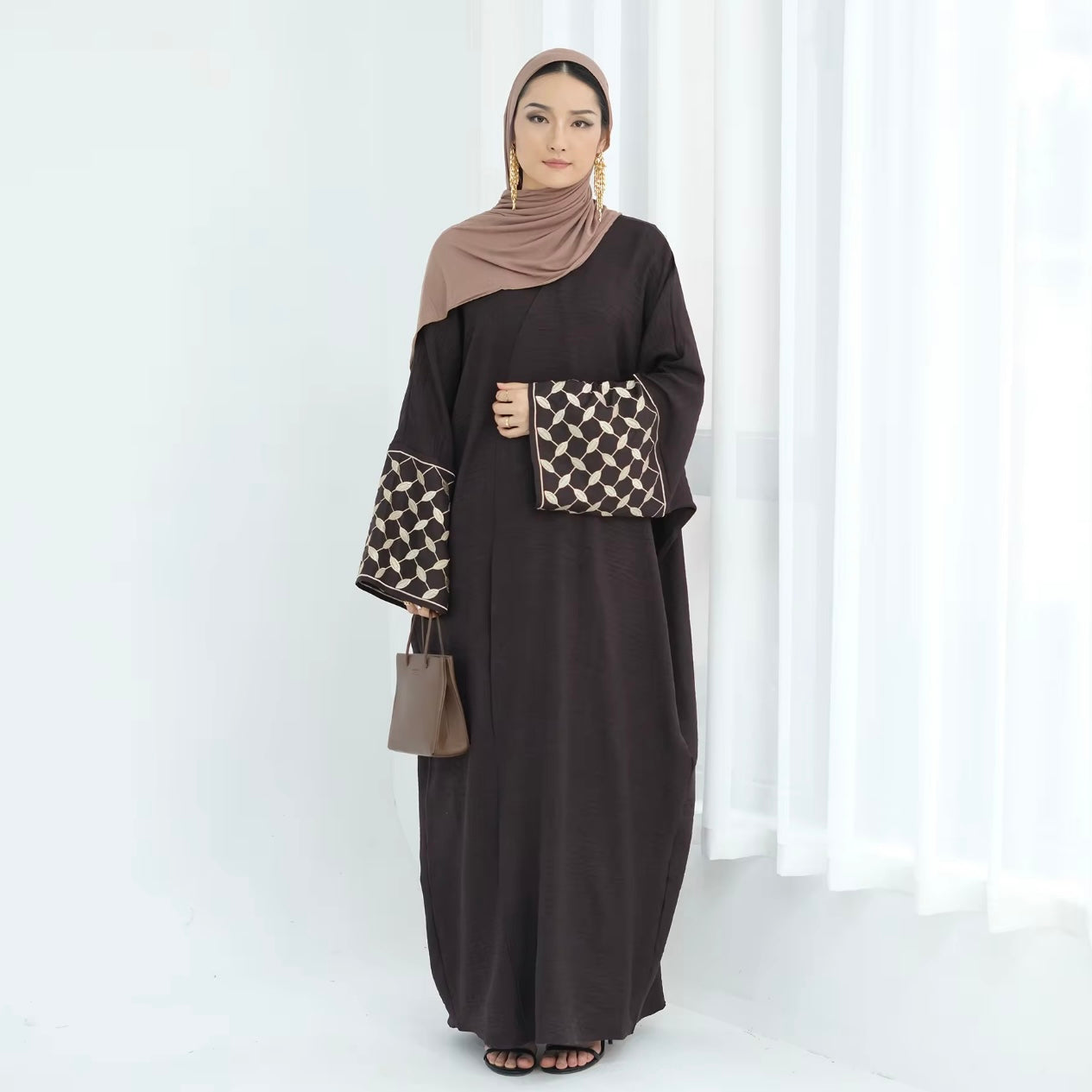 Woman wearing a dark brown abaya with patterned sleeves against a white background