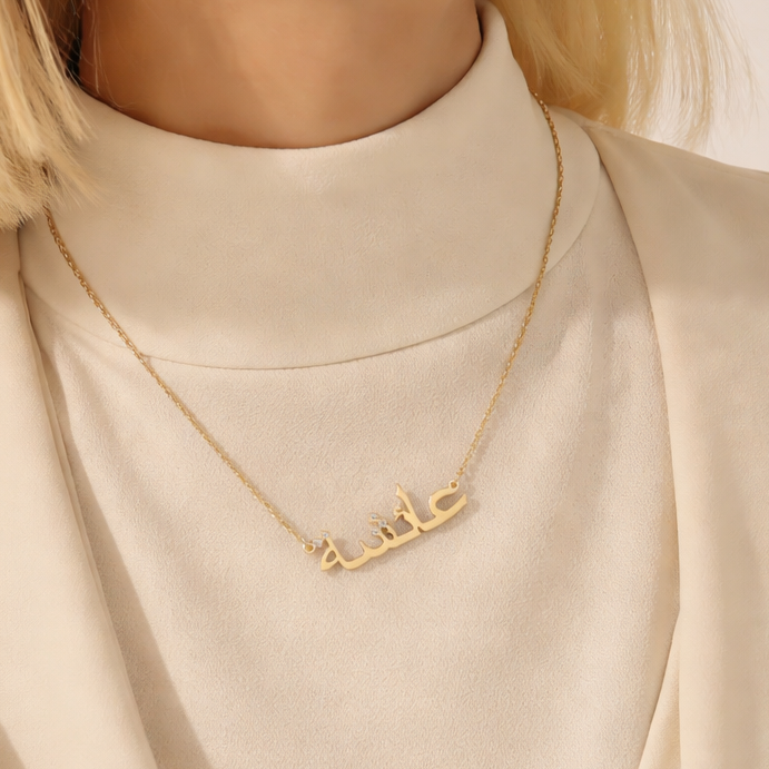 Gold necklace with Arabic script worn by a person in a beige outfit