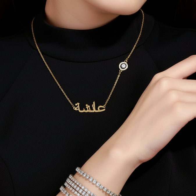 Woman wearing a gold necklace with a name pendant, black top, and silver bracelet.