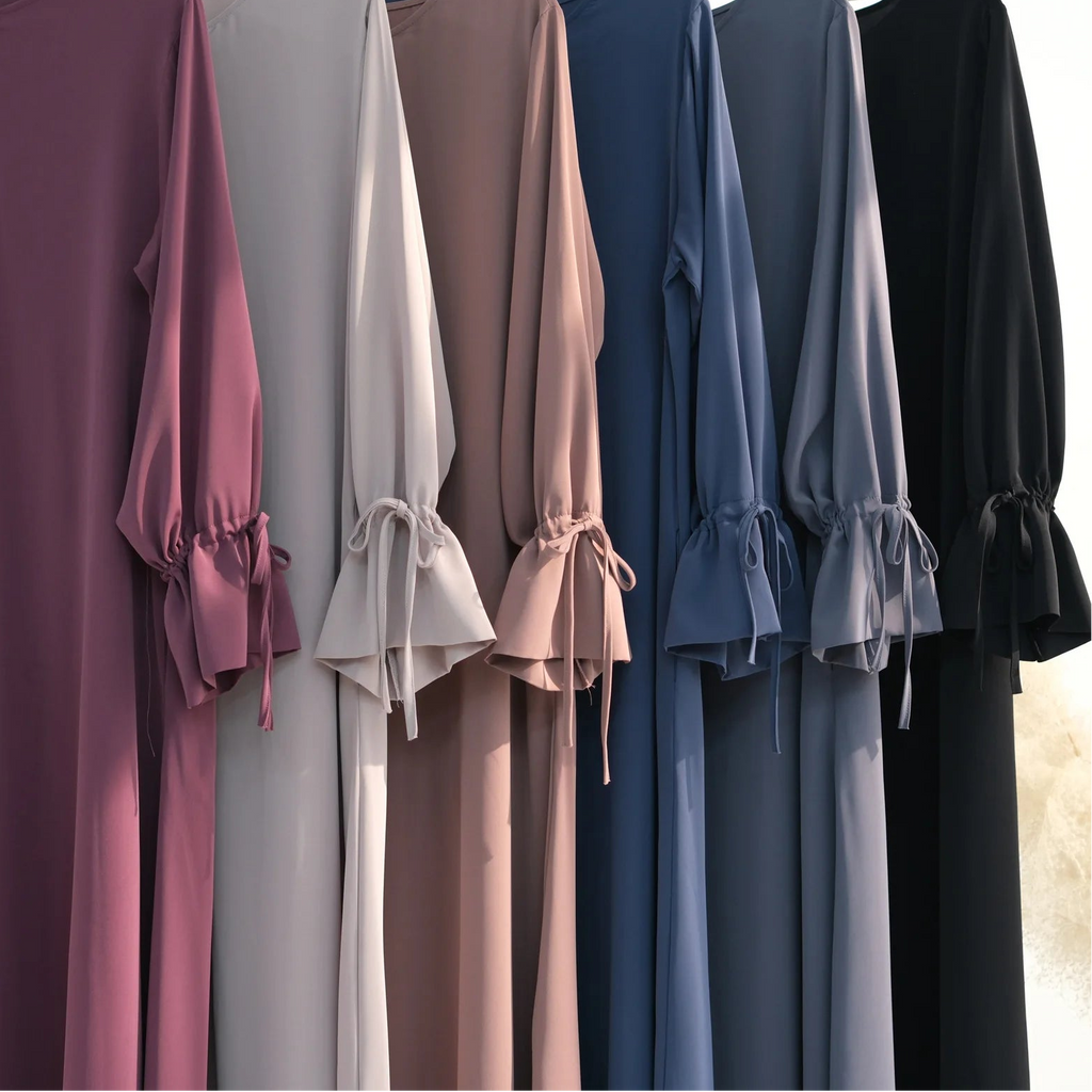 Row of long-sleeve abaya dresses in various colors on hangers against a neutral background