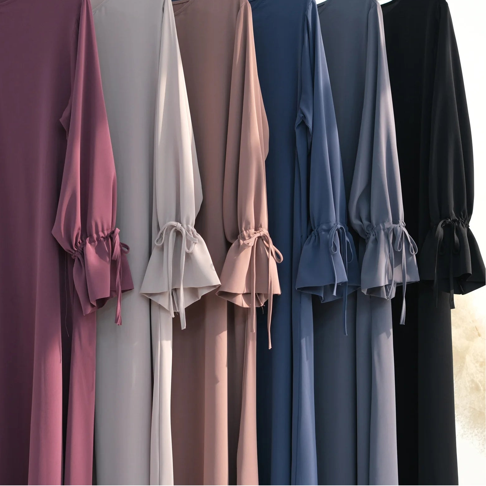 Row of long-sleeve abaya dresses in various colors on hangers against a neutral background