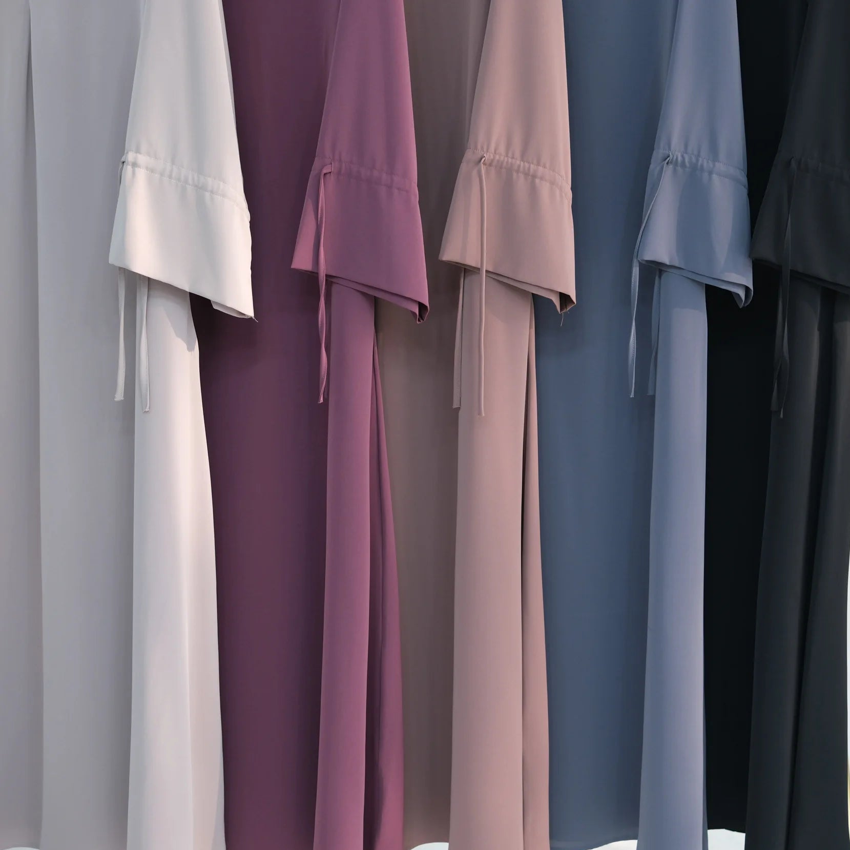 Set of long, flowing abayas in various colors hanging on a rack.