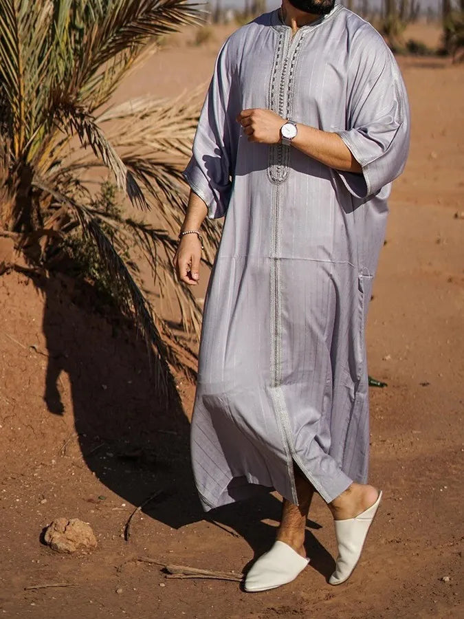 Person wearing a long light gray dress standing in a desert setting with a palm tree.
