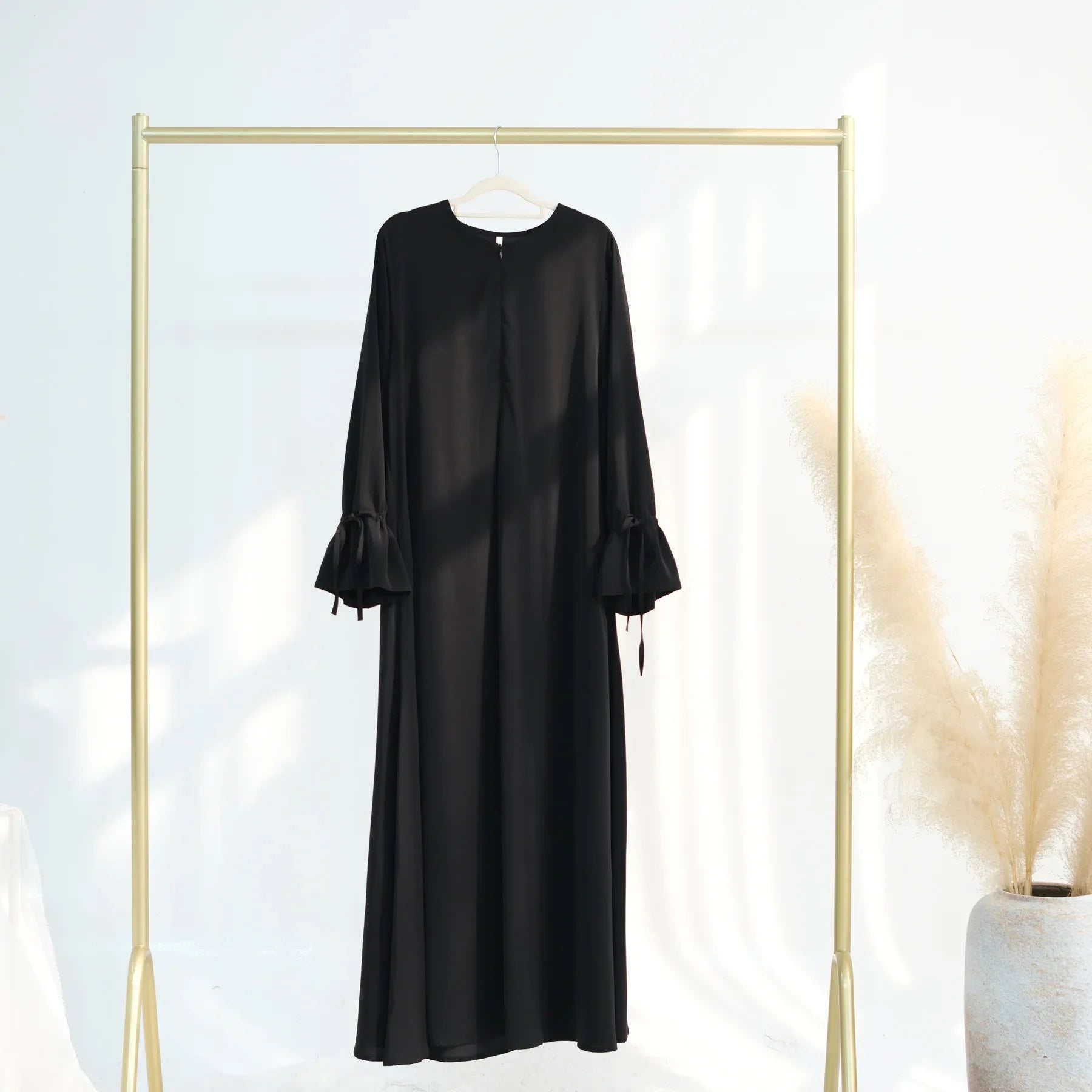 Long-sleeve abaya dress hanging on a gold rack against a white background