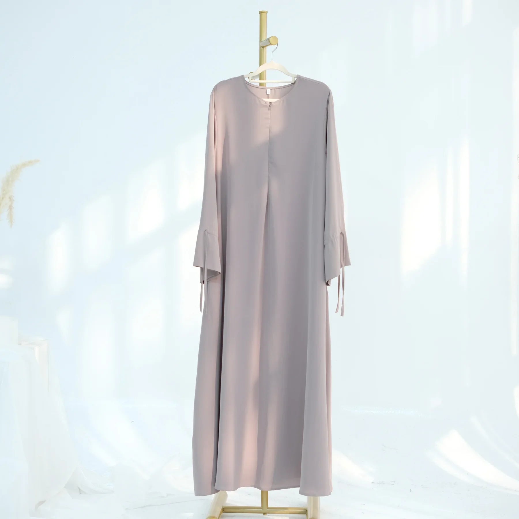 Long-sleeve abaya dress hanging on a gold rack against a white background
