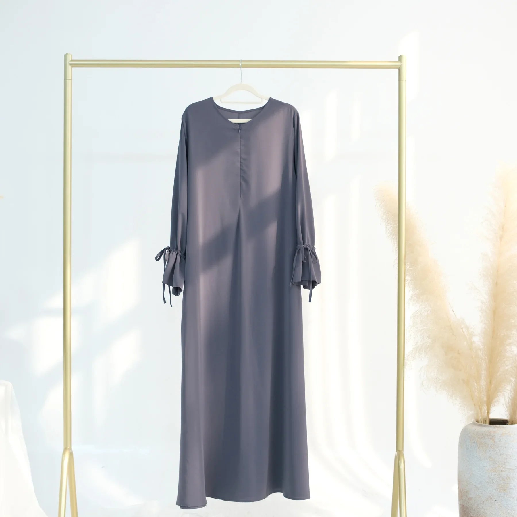 Long-sleeve abaya dress hanging on a gold rack against a white background